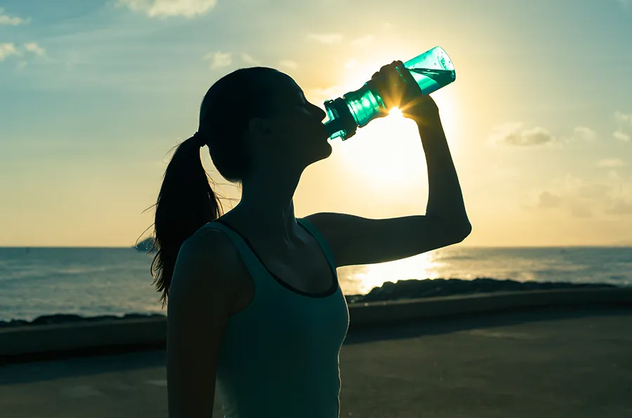 A woman hydrates during a beach run at sunset. Schedule natural detoxification treatment from Morgan Burns, APRN in Central Florida.