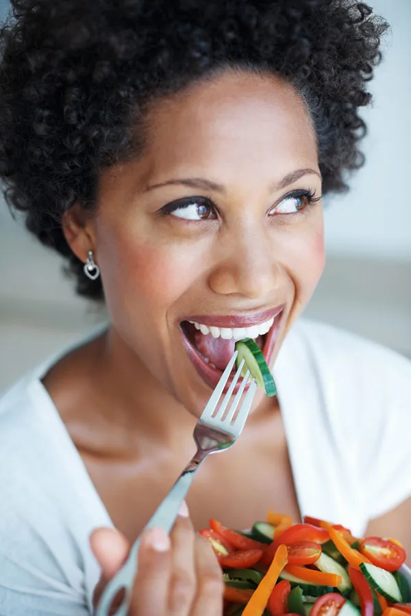 A Black woman smiles while eating a healthy salad. Get natural detoxification treatment from Morgan Burns, APRN in Central Florida.