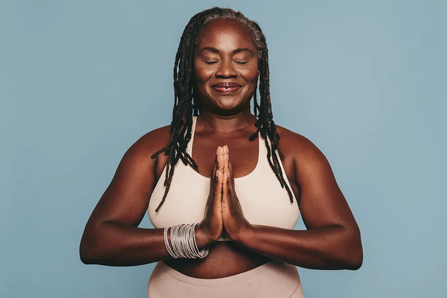 An older black woman with closed eyes holds her hands together in a yoga pose. Get treatment for pre-diabetes from Morgan Burns, APRN in Central Florida.