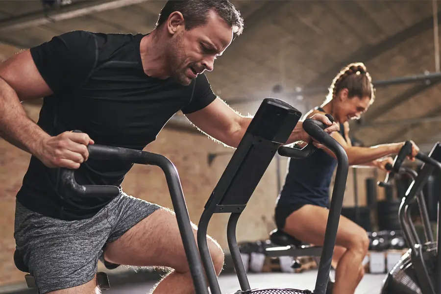 A couple in a brick gym work as hard as they can on exercise bikes, inspired by successful Tirzepatide treatment from Morgan Burns, APRN in Central Florida.