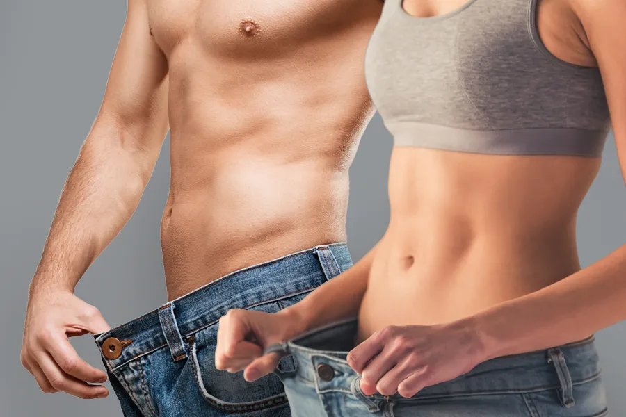A man and a woman with toned bodies hold their jeans away from their waists to show weight loss. Get weight loss peptide treatment from Morgan Burns, APRN in Central Florida.
