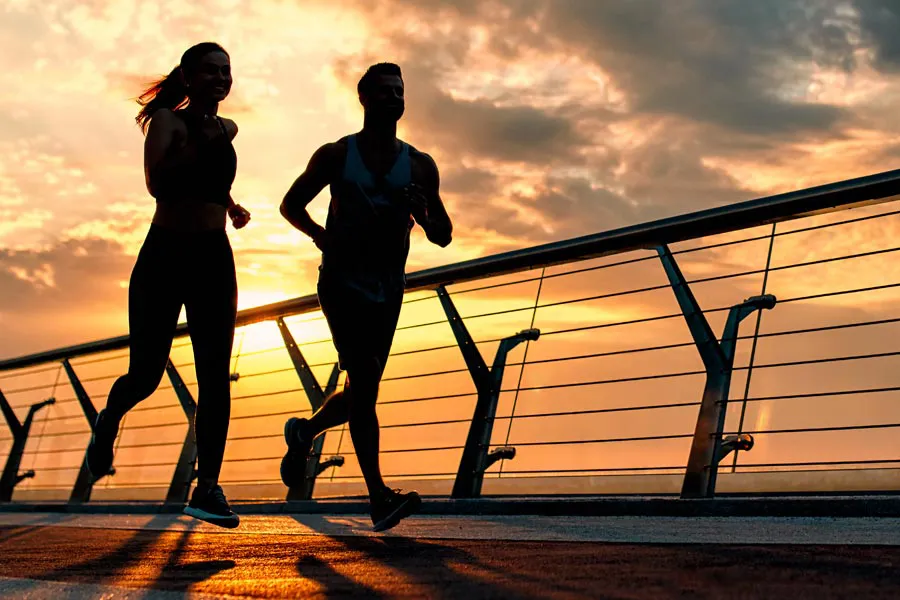 A couple running on a bridge, silhouetted by the sunrise. Get Amino Blend Vitamin Injection treatment from Christine Collins, MD in Westside/Beverly Hills.