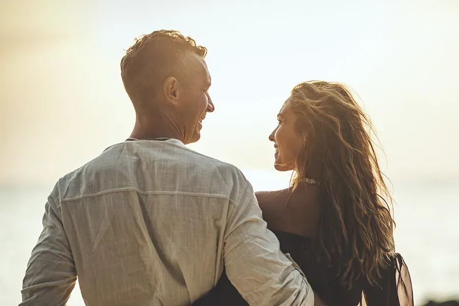 A couple gazes at each other on the beach at sunrise, viewed from behind. Schedule Anti-Aging treatment from Christine Collins, MD in Westside/Beverly Hills.