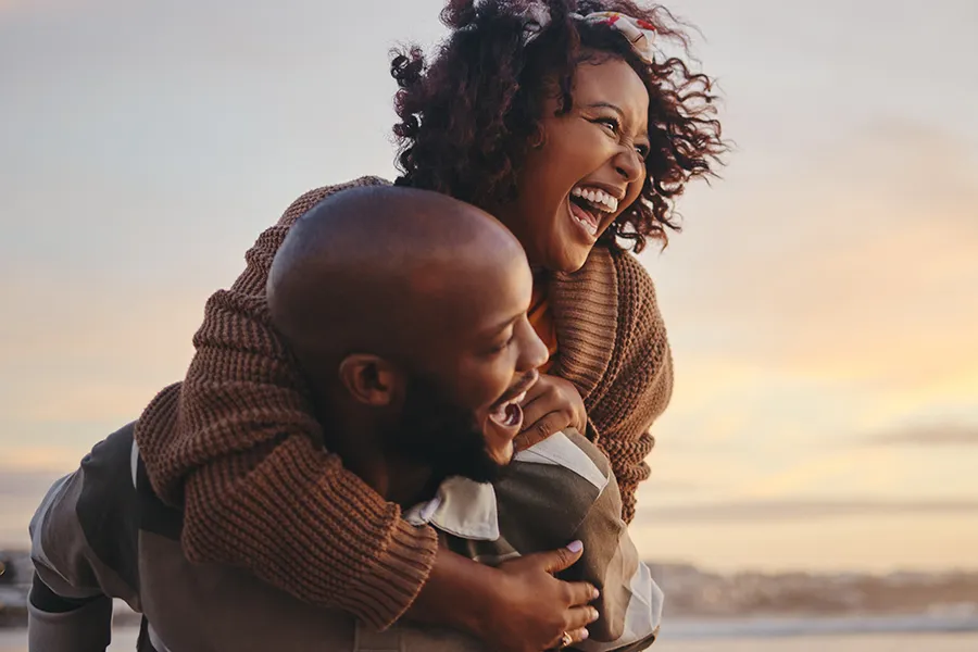 A middle-aged Black couple embrace playfully at the beach. Schedule BCAA Vitamin Injection treatment from Christine Collins, MD in Westside/Beverly Hills.