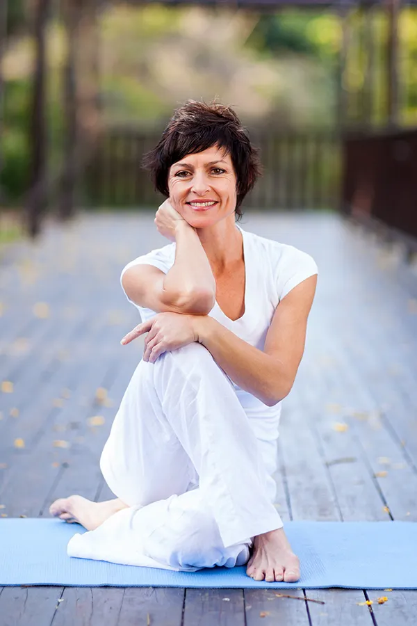 A middle-aged woman sits on a yoga mat. Get BCAA Vitamin Injection treatment from Christine Collins, MD in Westside/Beverly Hills.