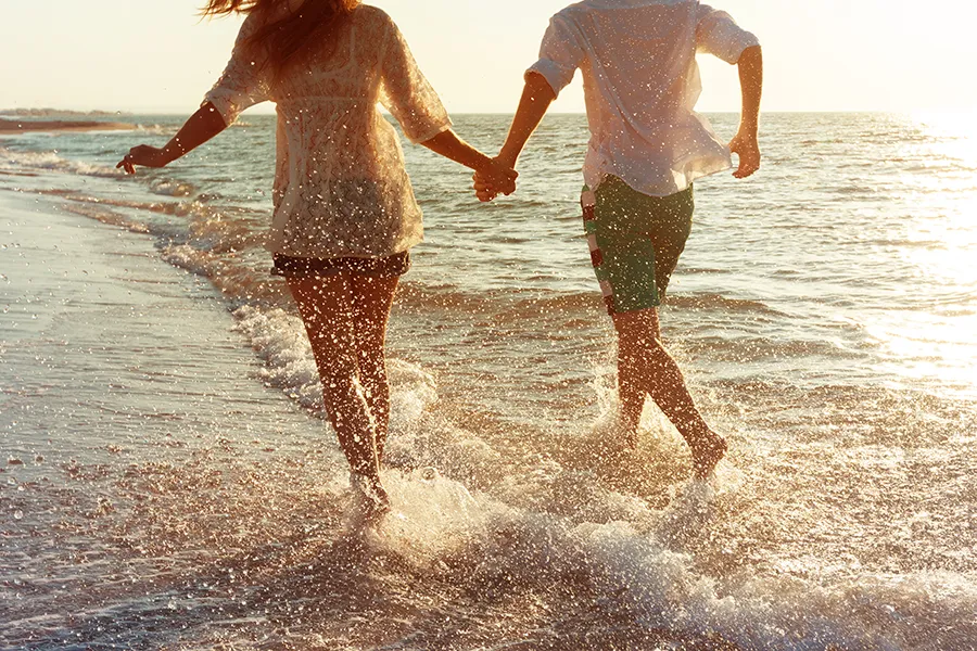 A couple run along the shore hand in hand. Schedule CVAC therapy from Christine Collins, MD in Westside/Beverly Hills.