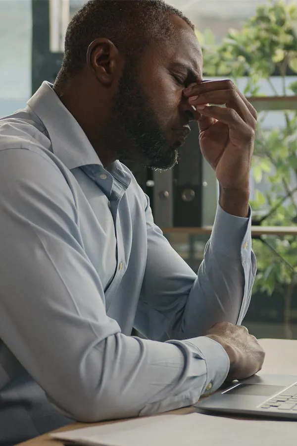 A black man rubbing the top of his nose at his desk, in need of chronic fatigue treatment from Christine Collins, MD in Westside/Beverly Hills.