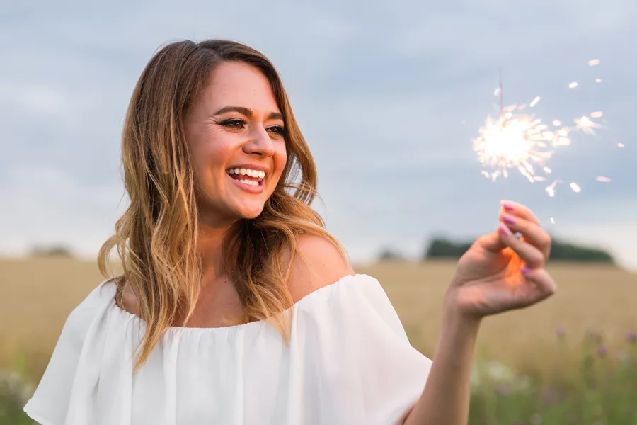 A cheerful young woman holding a lit sparkler in an open field at dusk satisfied with successful EMsella Pelvic Floor Strengthening treatment by Christine Collins, MD in Westside/Beverly Hills.