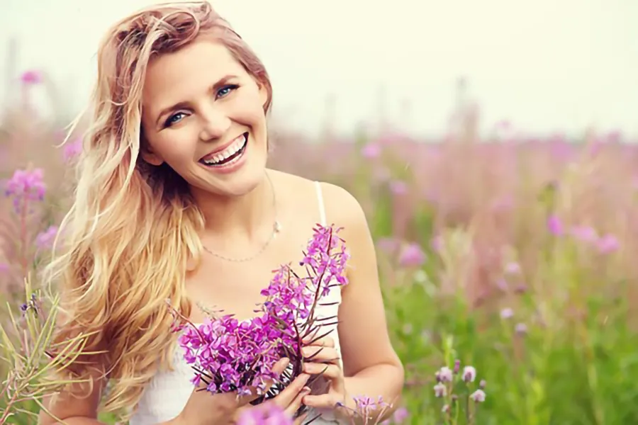 A smiling woman in a field holds a bunch of purple flowers. Get gynecology services from Christine Collins, MD in Westside/Beverly Hills.