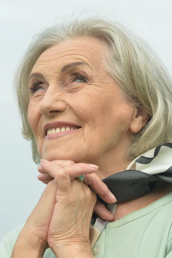 An older woman holds her hands together under her chin and looks up at a cool sky smiling. Get treatment for hot flashes and night sweats from Christine Collins, MD in Westside/Beverly Hills.