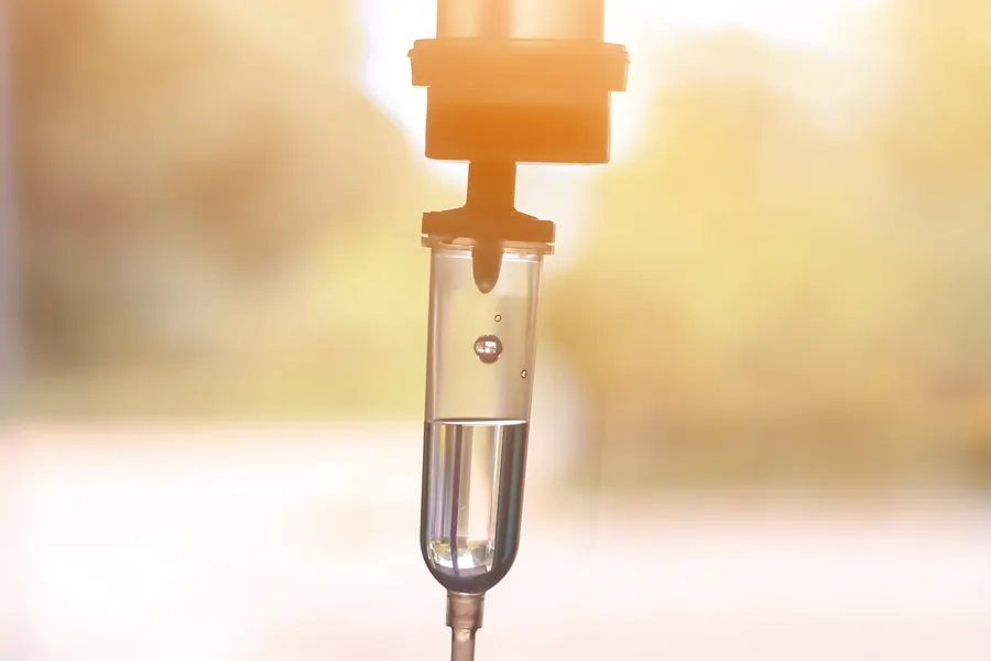 Close-up of an IV drip warmly lit by a window showing trees and a sunset, representing IV therapy from Christine Collins, MD in Westside/Beverly Hills.