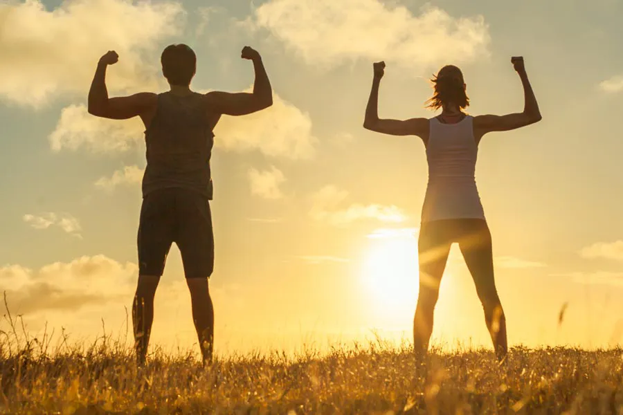 A couple flex their raised arms in the sunset. Schedule Tri-Immune Boost Injection treatments from Christine Collins, MD in Westside/Beverly Hills.