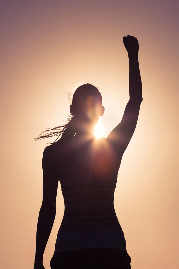 A woman raises her fist in the air, silhouetted by the sun. Get methylene blue IV therapy from Christine Collins, MD in Westside/Beverly Hills.
