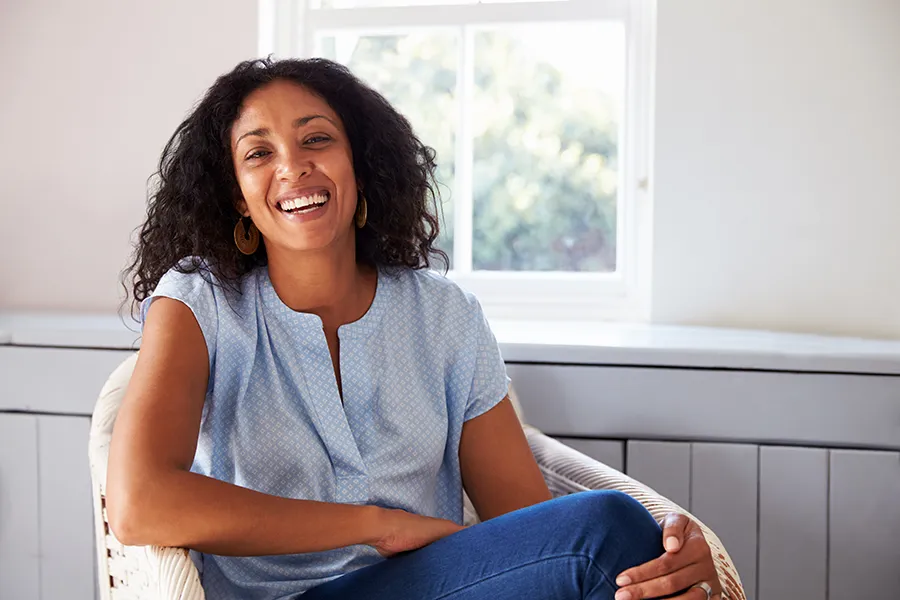 A happy Black woman sitting in a sun room. Get NAC Vitamin Injection treatment from Christine Collins, MD in Westside/Beverly Hills.