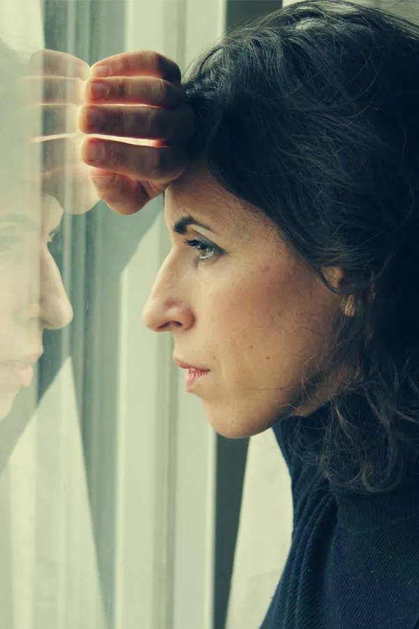 A brunette woman in a thin dark turtleneck looks out the window with a serious expression, suffering from PCOS. Get treatment for Polycistic Ovarian Syndrome/PCOS from Christine Collins, MD in Westside/Beverly Hills.