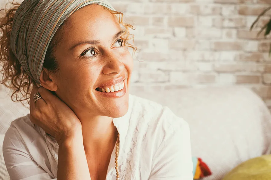 A mixed-race woman sits smiling in her living room. Schedule Vitamin B6 Injection treatment from Christine Collins, MD in Westside/Beverly Hills.