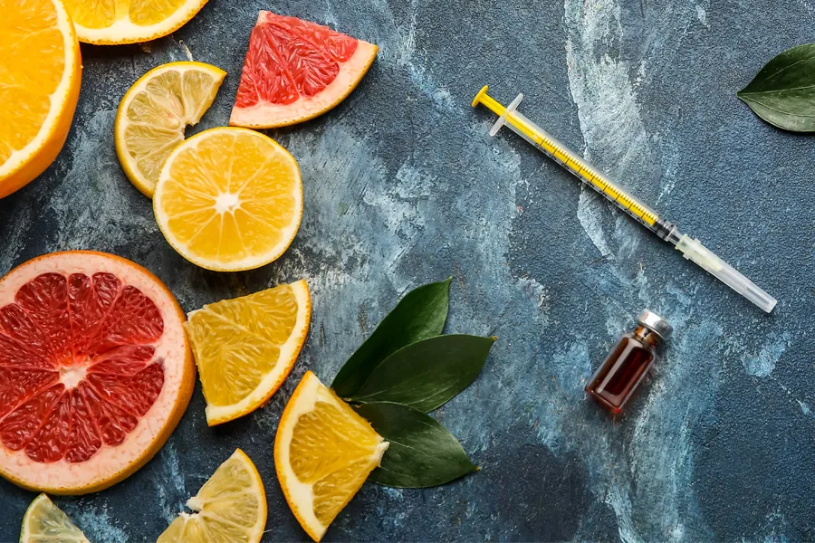 A gray marble countertop covered with sliced fruit and a syringe and vial, representing vitamin injections from Christine Collins, MD in Westside/Beverly Hills.