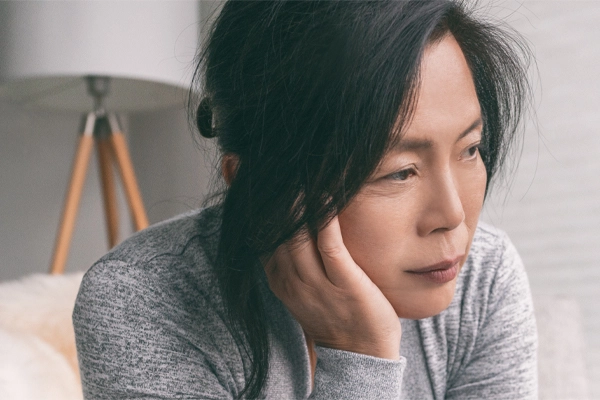 A middle-aged asian woman sitting on her couch, resting her head on her hand, suffering from adrenal fatigue. Get treatment for adrenal fatigue syndrome from Frank Lanzisera, D.C. in Tampa Bay Metro.