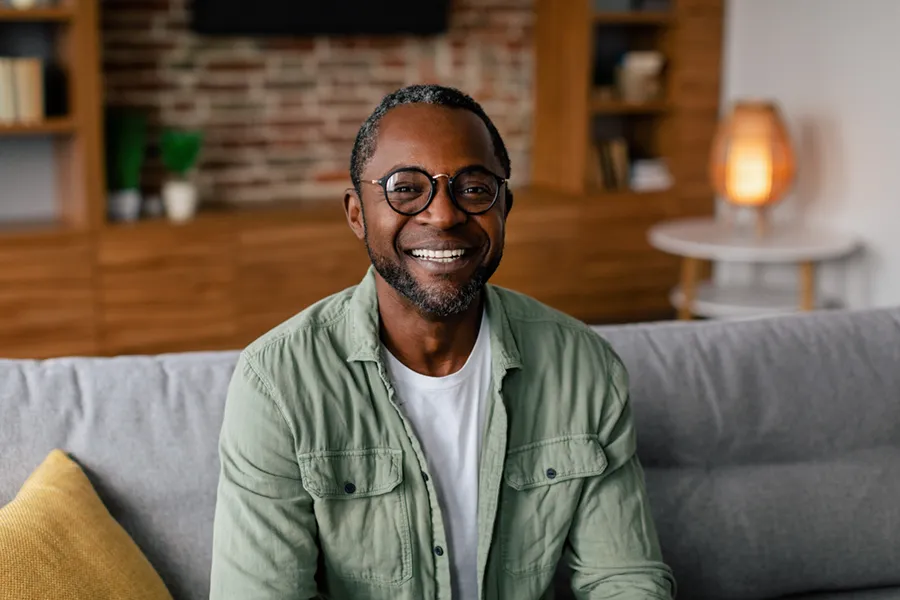 A middle aged black man in a green button up shirt sits on his couch smiling, happy with his treatment for andropause and low testosterone from Frank Lanzisera, D.C. in Tampa Bay Metro.