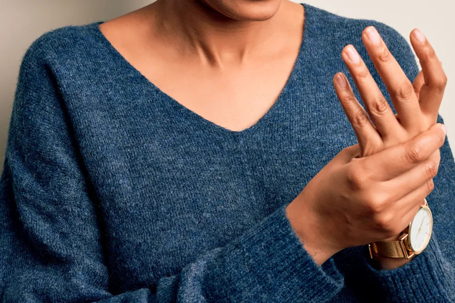 Close up of a woman in a blue sweater massaging one aching hand with the other. Get help for arthritis from Frank Lanzisera, D.C. in Tampa Bay Metro.