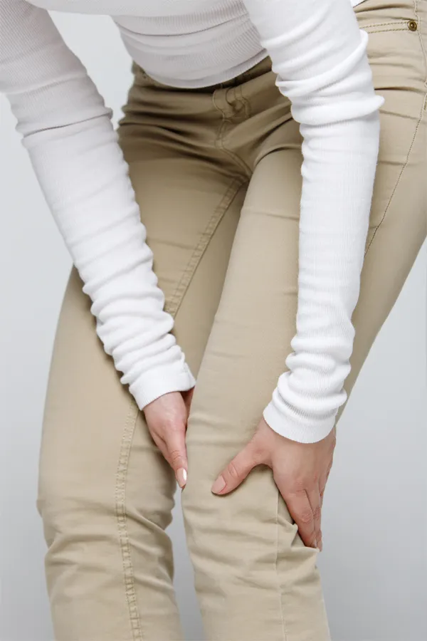 A woman wearing a white long-sleeve shirt and tan pants, clutching her knee, suffering from arthritis. Get arthritis treatment from Frank Lanzisera, D.C. in Tampa Bay Metro.