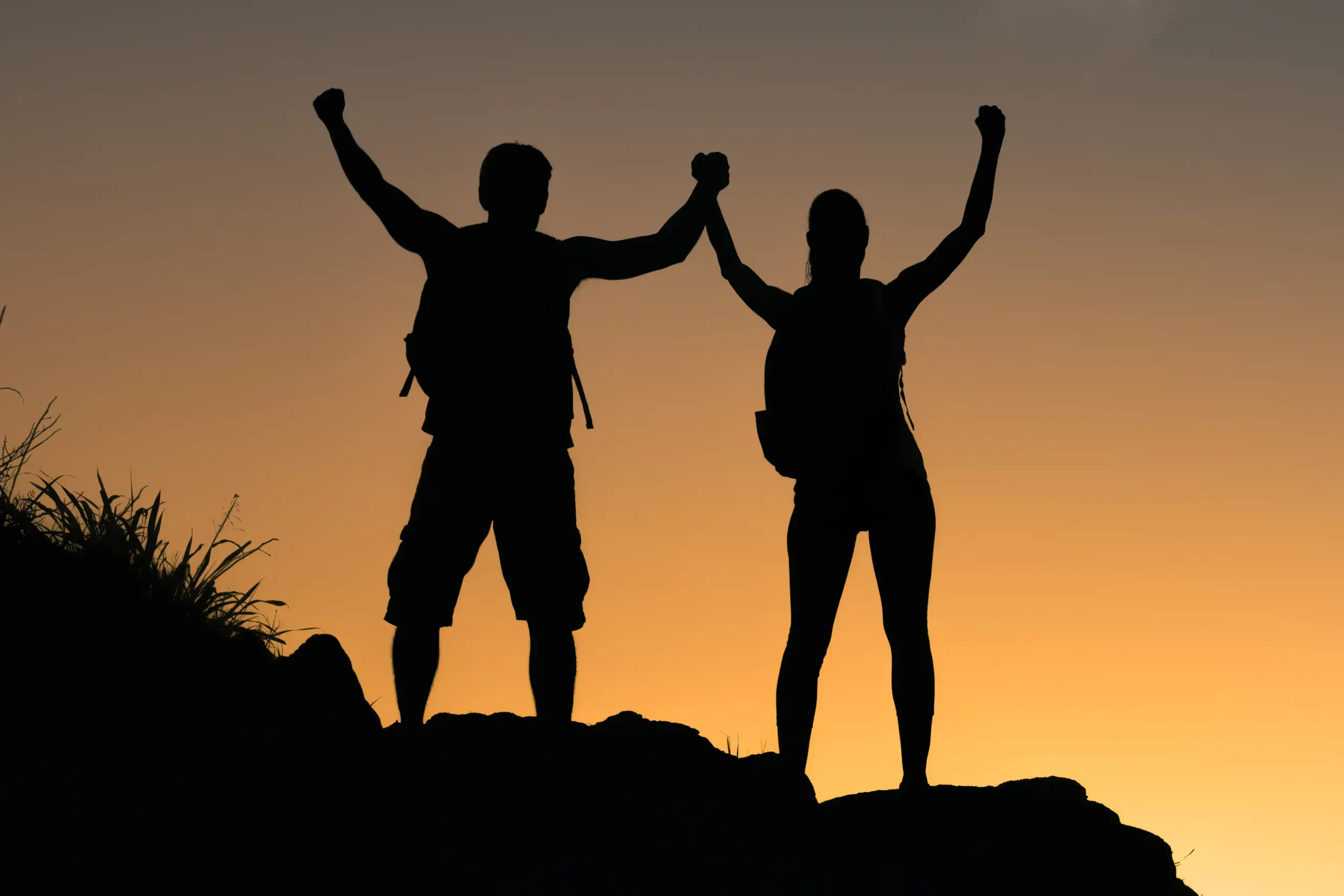 A couple completing a mountain climb hold their arms up to the sunset. Get IV therapy for weight loss from Frank Lanzisera, D.C. in Tampa Bay Metro.