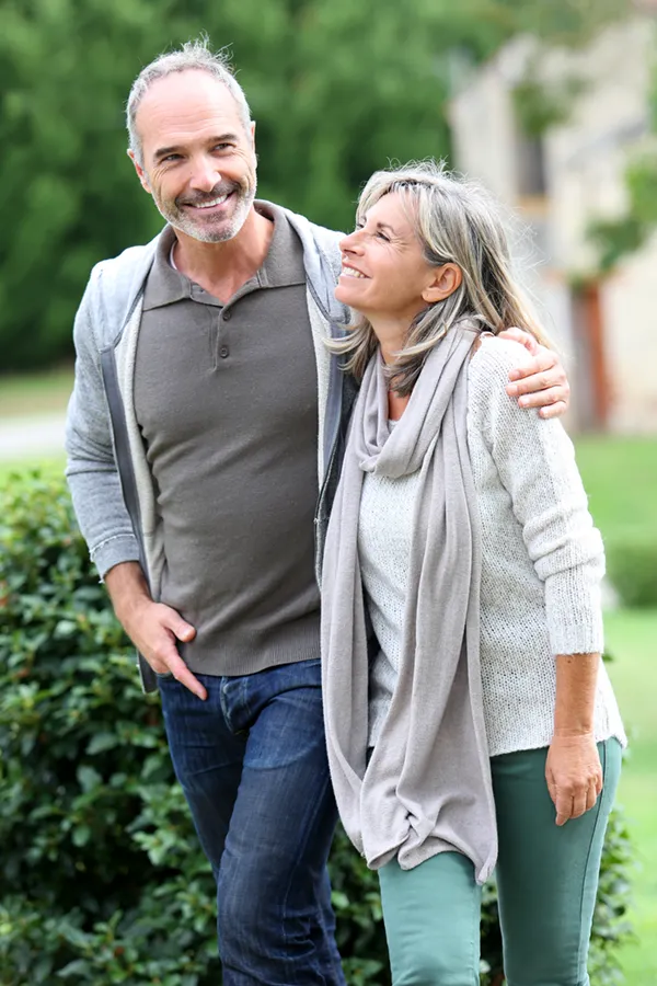 A mature couple in gray toned clothes and jeans walk happily outside, happy with their successful bioidentical hormone treatments from Frank Lanzisera, D.C. in Tampa Bay Metro.