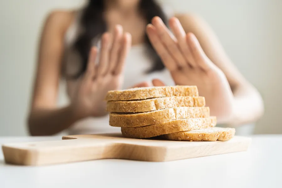 Close up of a stack of bread slices on a cutting board with a woman's hands behind them, refusing to eat. Get treatment for Celiac Disease from Frank Lanzisera, D.C. in Tampa Bay Metro.