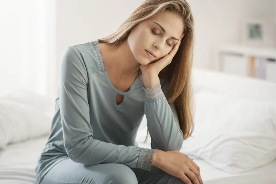 A woman sits on the edge of her bed with her head in her hands. Schedule treatment for depression from Frank Lanzisera, D.C. in Tampa Bay Metro.