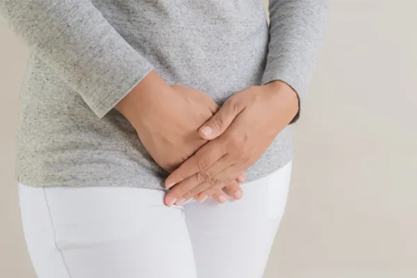 Close up of a woman in a gray shirt and white pants holding her hands below her abdomen in discomfort. Get treatment for fibroids from Frank Lanzisera, D.C. in Tampa Bay Metro.