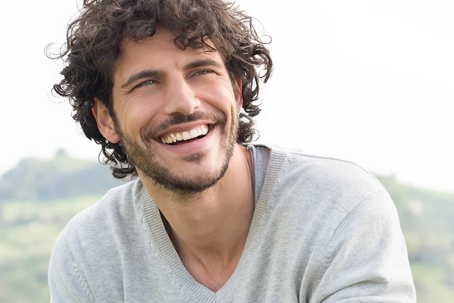 A man with radiant curly hair and a confident smile looks to the horizon. Frank Lanzisera, D.C. in Tampa Bay Metro offers effective therapies to support hair regrowth and scalp health to treat hair loss.