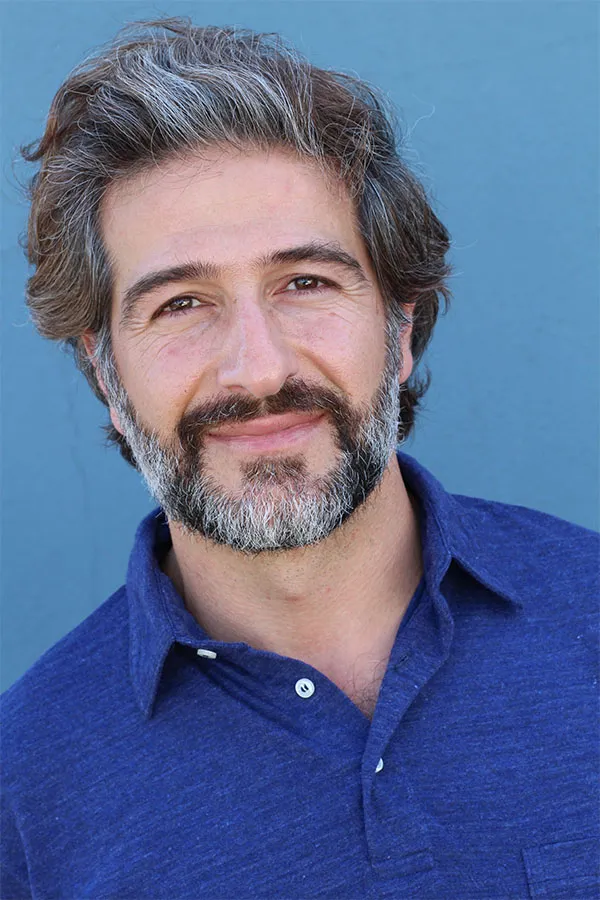 Image of a cheerful man with a bright smile and curly hair against a natural landscape. Frank Lanzisera, D.C. provides personalized hair loss treatments in Tampa Bay Metro.