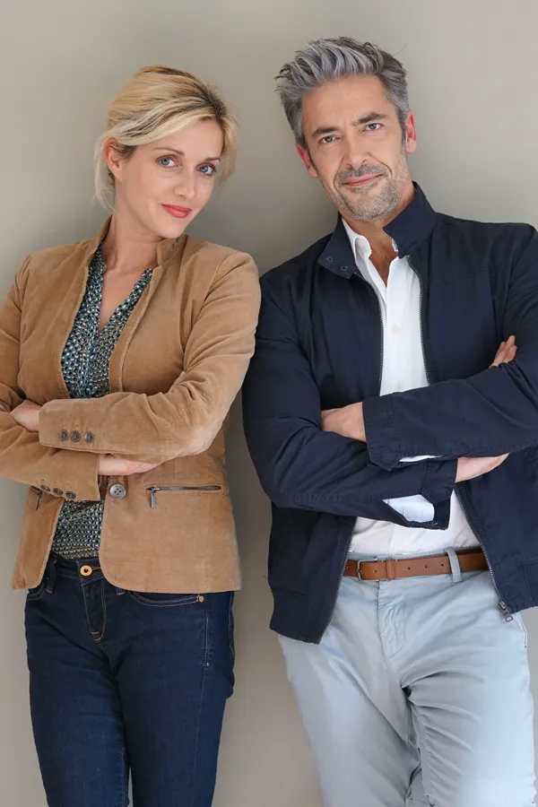 A middle-aged couple stand against a wall smiling with folded arms. Get hyperthyroidism treatment from Frank Lanzisera, D.C. in Tampa Bay Metro.
