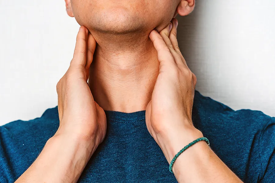 A man in a dark teal shirt rubs the lymph nodes on his neck. Get hypothyroidism treatment from Frank Lanzisera, D.C. in Tampa Bay Metro.
