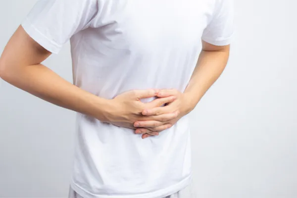 A person holding their stomach in visible discomfort against a plain background. Frank Lanzisera, D.C. treats irritable bowel syndrome with functional medicine in Tampa Bay Metro.