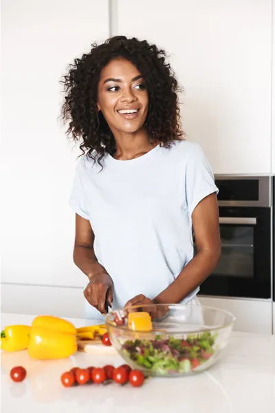 Image featuring a smiling woman chopping vegetables for a salad in a bright, white kitchen. Frank Lanzisera, D.C. offers Irritable Bowel Syndrome Treatment and Digestive Support in Tampa Bay Metro.