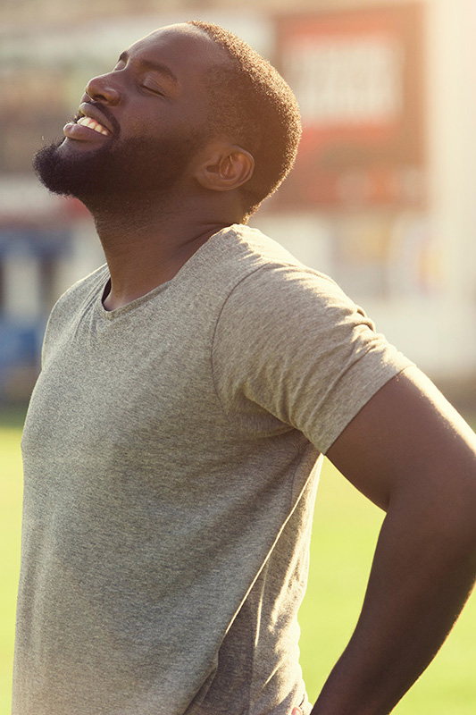 A black man in a gray t-shirt and smiles, looking up with closed eyes after a satisfying workout. Get treatment for lean muscle loss and recovery from Frank Lanzisera, D.C. in Tampa Bay Metro.
