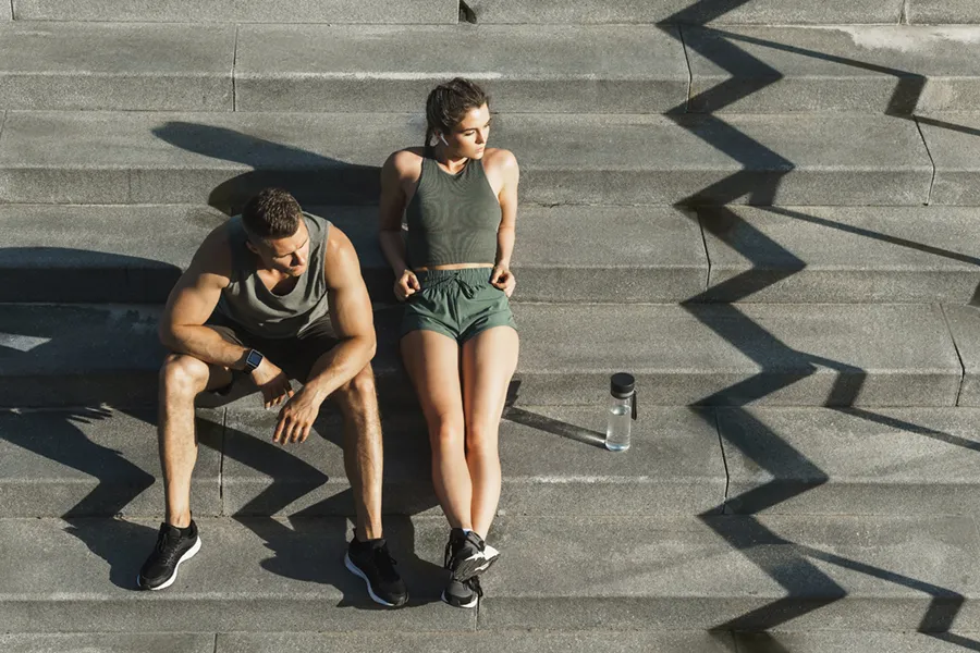 A couple in gray and green track clothes resting after a workout on stone steps, happy with their weight loss plans from Frank Lanzisera, D.C. in Tampa Bay Metro.