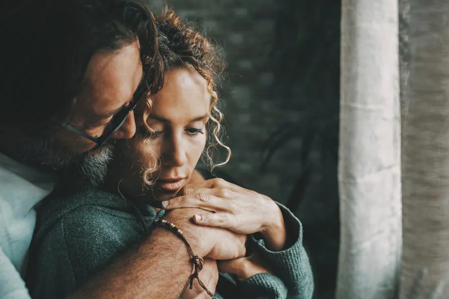 A man embraces a woman from behind in a dimly lit room, their somber expressions showing concerns about a neurodegenerative disease they will get treated by Frank Lanzisera, D.C. in Tampa Bay Metro.