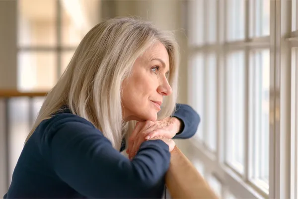 A middle-aged woman with with a somber expression stares out the window. Get treatment for Premenstrual Dysphoric Disorder from Frank Lanzisera, D.C. in Tampa Bay Metro.