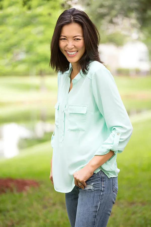 A middle-aged brunette woman in a light green button-up shirt stands outside smiling, happy with her perimenopause treatment from Frank Lanzisera, D.C. in Tampa Bay Metro.