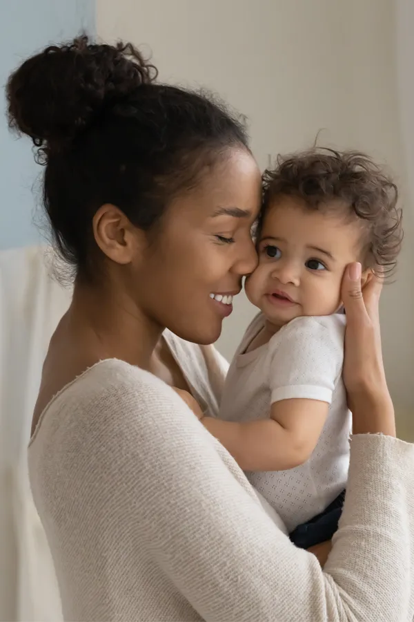 A black woman happily touches her forehead to her infant's head. Get treatment for postpartum hormone imbalance from Frank Lanzisera, D.C. in Tampa Bay Metro.