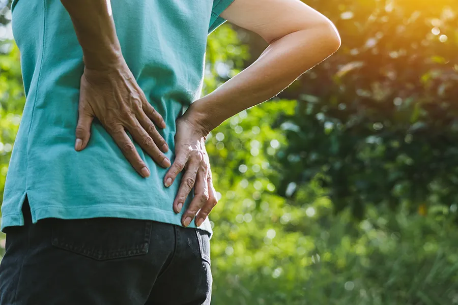 A woman holds her lower back in pain. Schedule Regenerative Medicine for Back Pain from Frank Lanzisera, D.C. in Tampa Bay Metro.