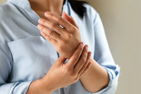 Close up of a woman in a blue blouse rubbing her wrist. Get rheumatoid arthritis treatment from Frank Lanzisera, D.C. in Tampa Bay Metro.