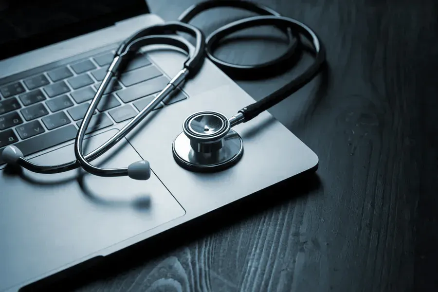 An open laptop with a stethoscope lying on it on a wooden table, symbolizing telemedicine care from Frank Lanzisera, D.C. in Tampa Bay Metro.
