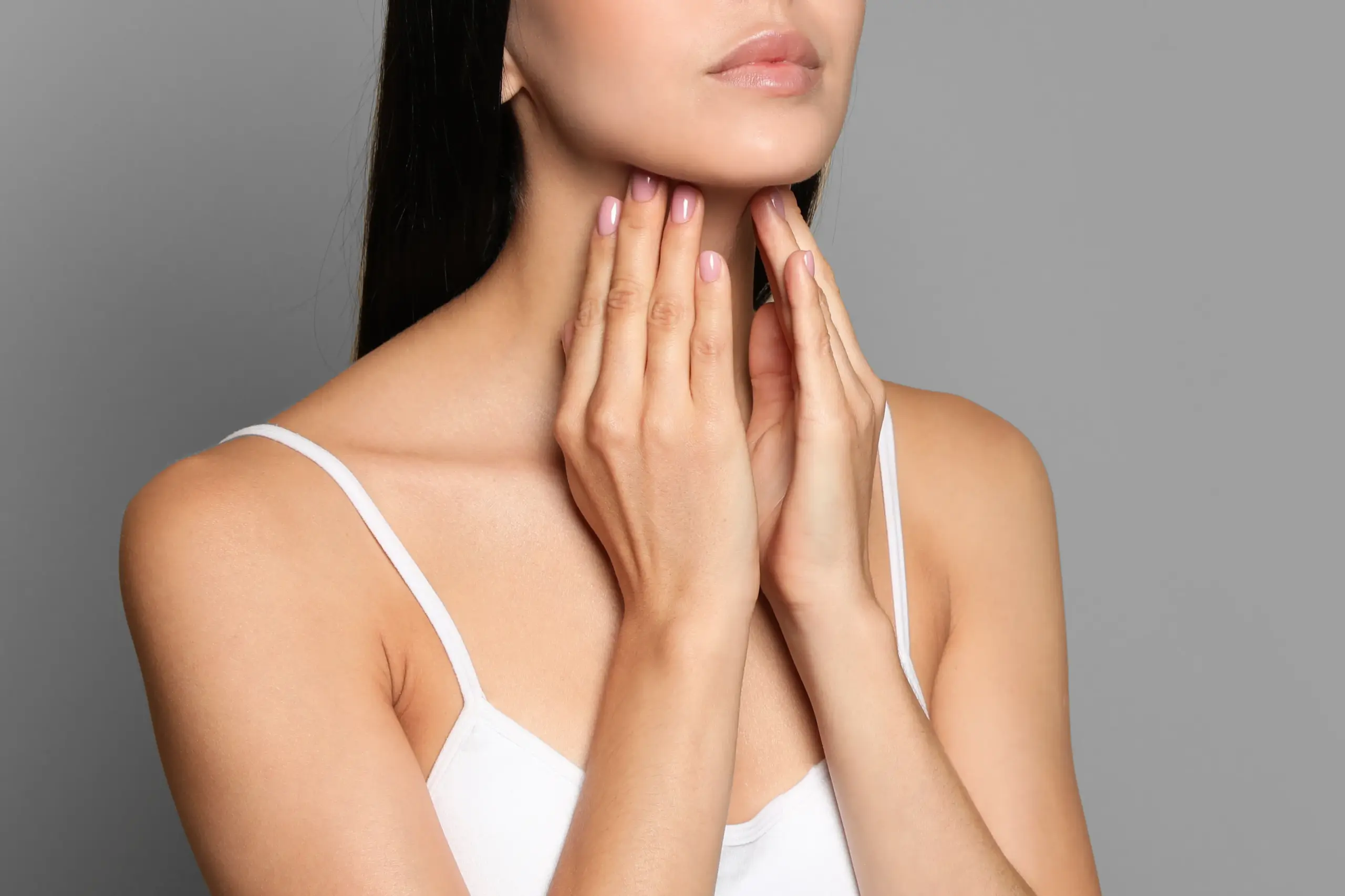 A woman in a white tank top touches her neck looking for signs of thyroid disorder. Get help for thyroid disorders from Frank Lanzisera, D.C. in Tampa Bay Metro.