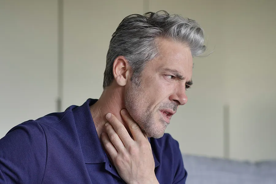 A man touches his throat with concern. Get treatment for thyroid symptoms from Frank Lanzisera, D.C. in Tampa Bay Metro.