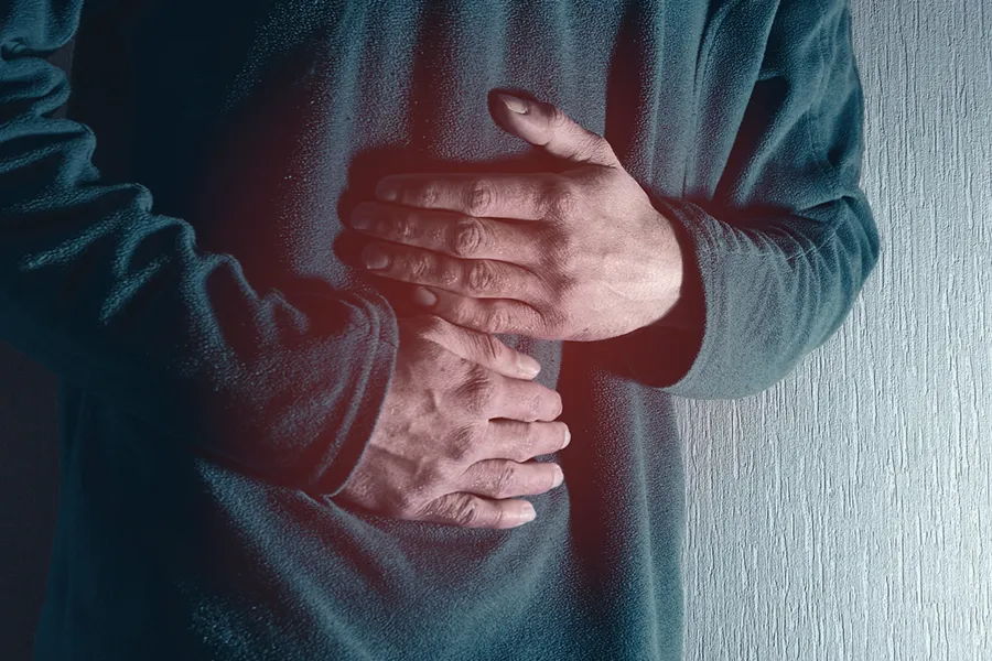 Close-up of the midsection of a man in a green sweater clutching his gut in pain. Get treatment for Ulcerative Colitis from Frank Lanzisera, D.C. in Tampa Bay Metro.