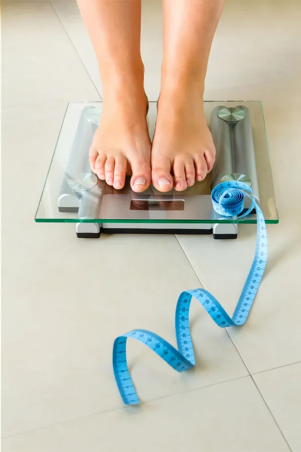 Close-up of a woman's feet standing on a scale, with measuring tape by her toes, getting treatment for weight loss resistance from Frank Lanzisera, D.C. in Tampa Bay Metro.